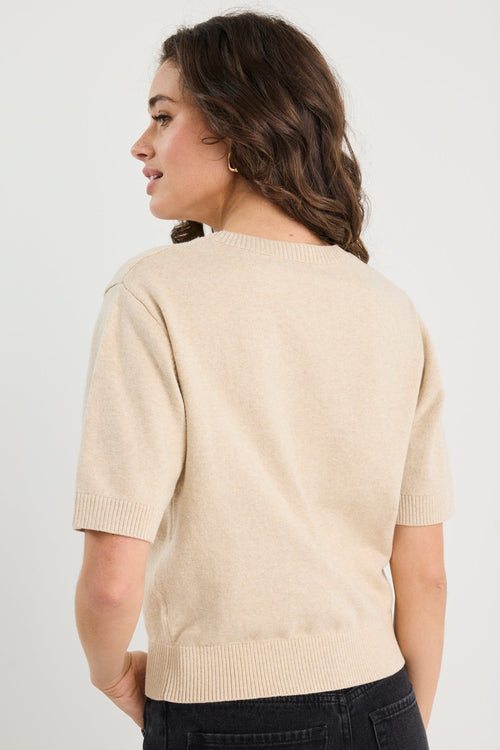 Woman wearing a beige sweater and black pants against a plain background