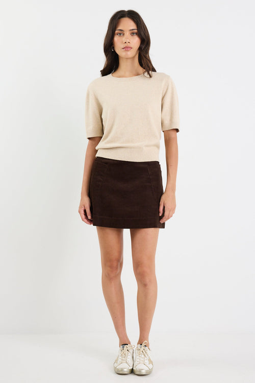 Woman wearing a beige sweater and brown skirt on a white background