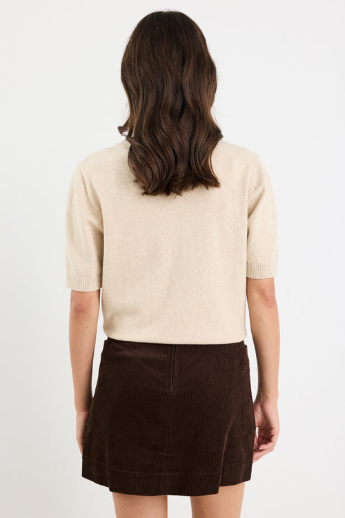 Person wearing a beige sweater and brown skirt on a white background