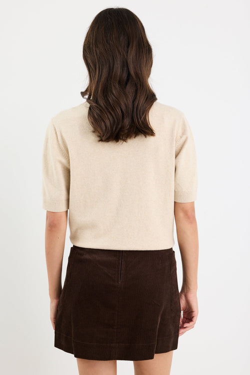Person wearing a beige sweater and brown skirt on a white background