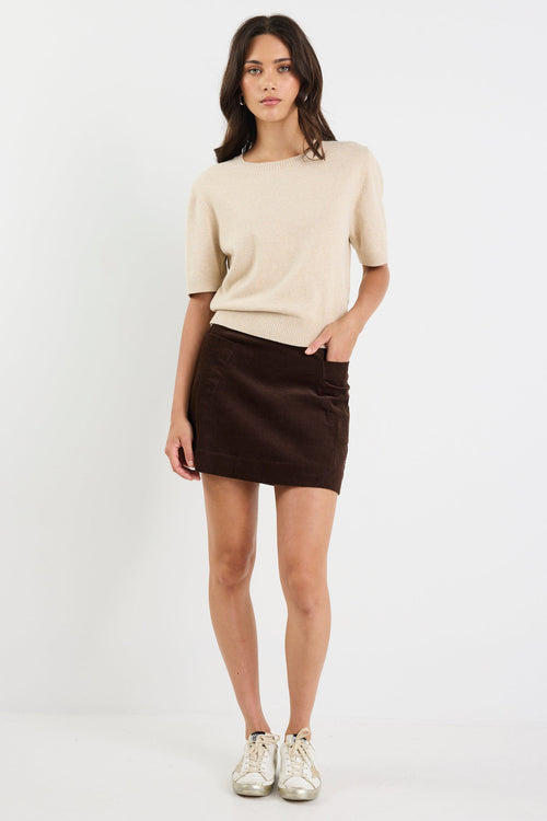 Woman wearing a beige top and black skirt on a white background