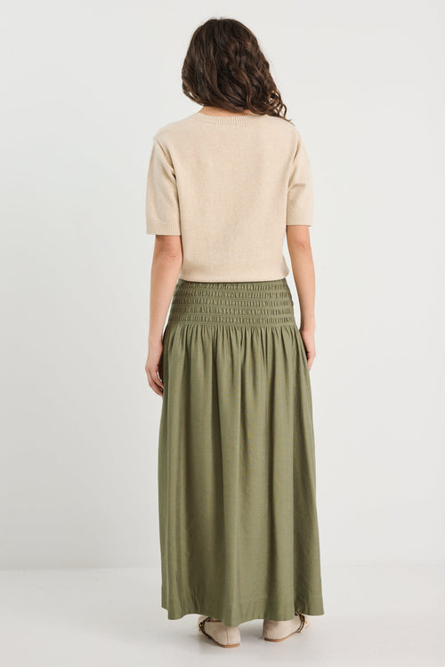 Woman wearing a beige top and green skirt on a white background