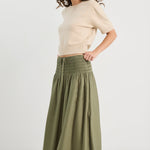 Woman wearing a beige sweater and green skirt on a white background