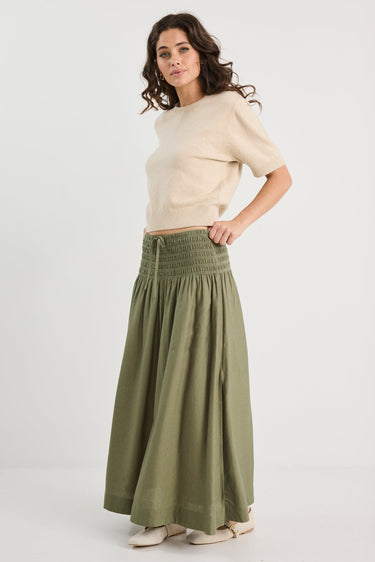 Woman wearing a beige sweater and green skirt on a white background