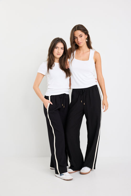 Two women wearing matching black pants with white stripes on a white background