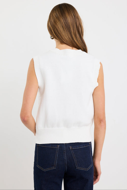 Woman wearing an ivory sleeveless knit vest top with gold button front closure and a crew neckline, styled with dark indigo jeans.