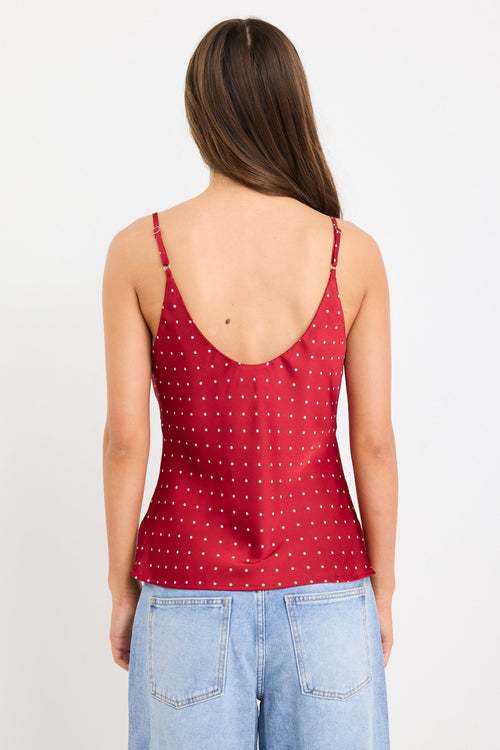 Woman wearing a red satin cami with white polka dots, bias-cut fit, and thin straps, styled with light blue jeans.