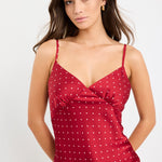 Woman wearing a red satin cami with white polka dots, bias-cut fit, and thin straps, styled with light blue jeans.