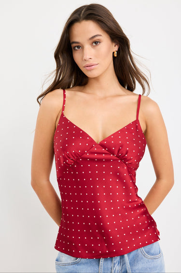 Woman wearing a red satin cami with white polka dots, bias-cut fit, and thin straps, styled with light blue jeans.