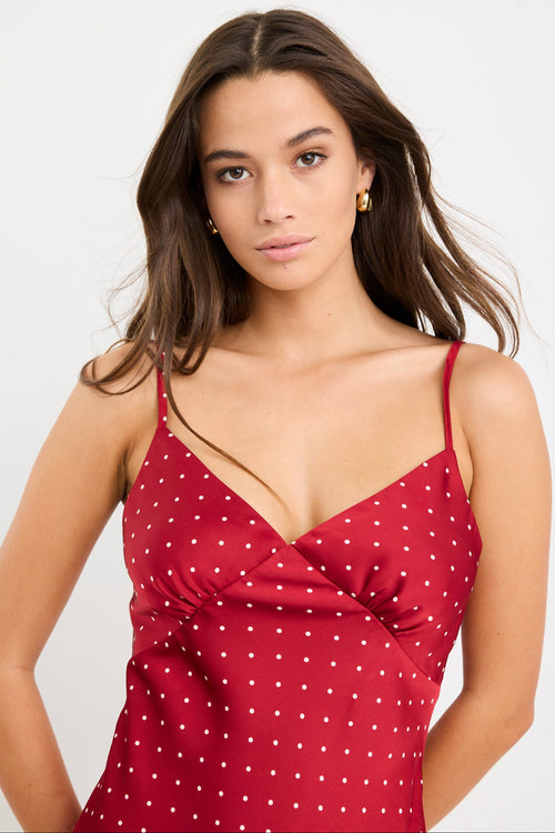 Woman wearing a red satin cami with white polka dots, bias-cut fit, and thin straps, styled with light blue jeans.