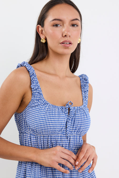 A sleeveless electric blue and white gingham mini dress with tiered detailing, tie-front feature, and a flattering fit. Fully lined for comfort, made from a 50% Cotton and 50% Viscose blend.