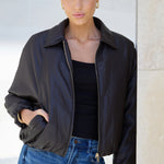 Woman wearing a black jacket and blue jeans against a neutral background