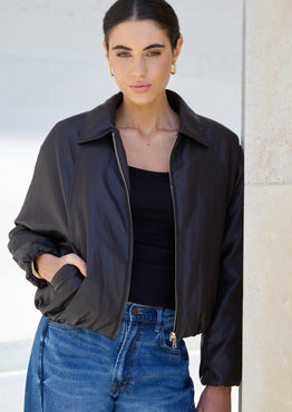 Woman wearing a black jacket and blue jeans against a neutral background