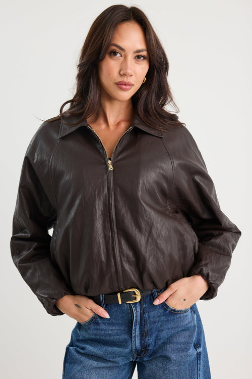 Woman wearing a brown leather jacket and blue jeans on a white background