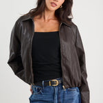 Woman wearing a black leather jacket, black top, and blue jeans on a white background