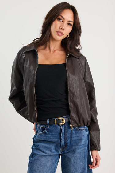 Woman wearing a black leather jacket, black top, and blue jeans on a white background