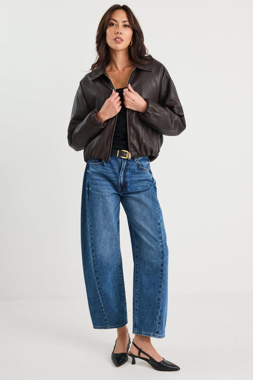 Woman wearing a brown leather jacket and blue jeans on a white background