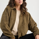 Woman wearing a khaki mock suede zip-up jacket with a soft, textured finish and a relaxed fit, styled over a beige knit top and black jeans.