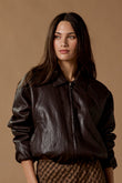 Woman wearing a black leather jacket and patterned skirt against a brown background