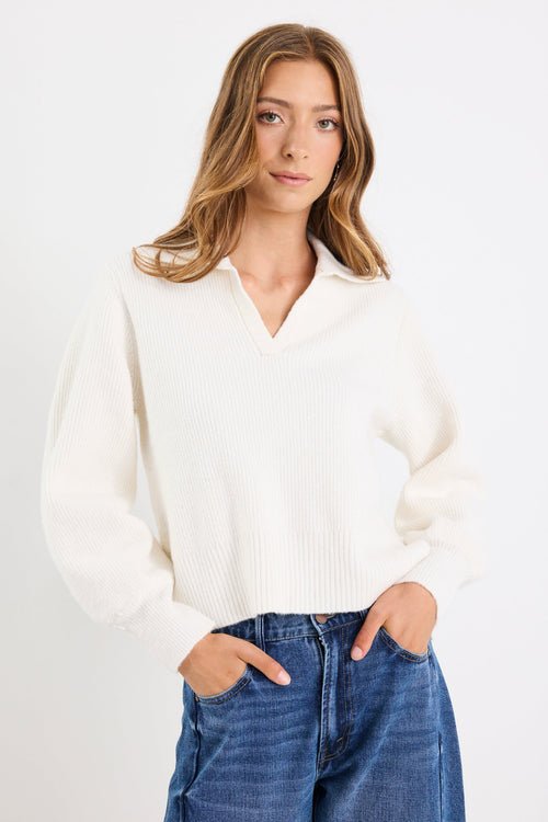 Woman wearing a white sweater and blue jeans against a plain background