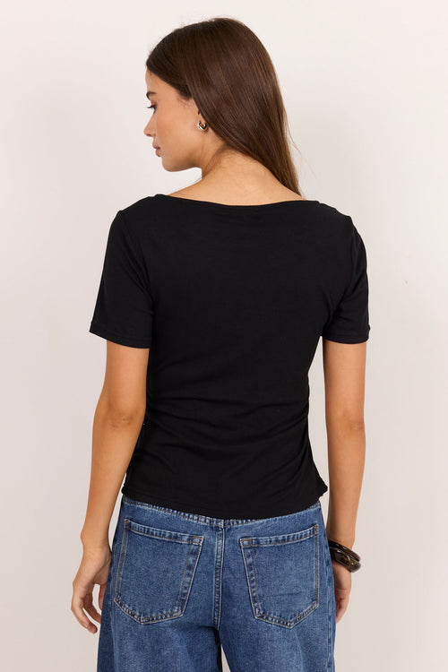 A woman shown from the back wearing a black short-sleeve boat-neck t-shirt and blue jeans, standing against a plain off-white background.