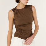 Woman wearing a brown sleeveless top with a knot detail on a white background