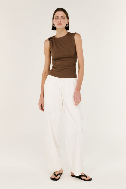 Woman wearing a brown sleeveless top and white pants on a white background