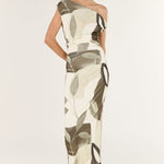 Woman wearing a one-shoulder dress with a leaf pattern on a white background