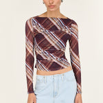 Woman wearing a patterned long-sleeve top and light blue jeans on a white background