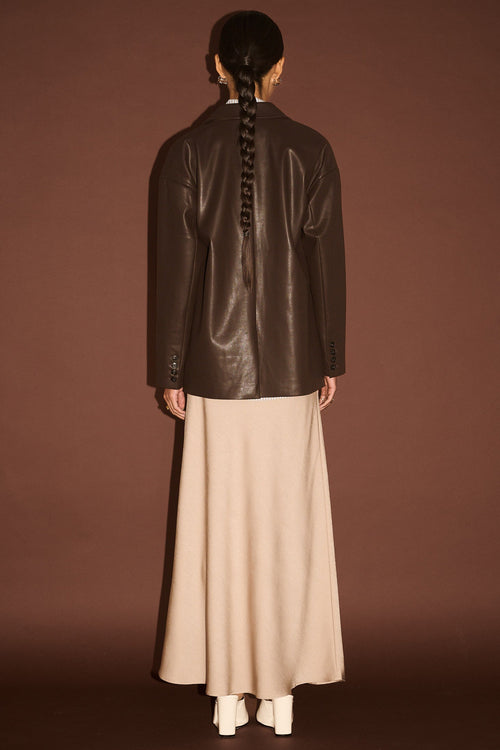 Person wearing a dark leather jacket and beige pants against a brown background