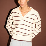 Woman wearing a striped sweater and light jeans against a brown background