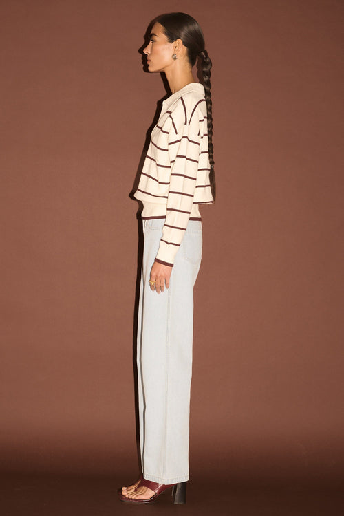 Woman wearing a striped sweater and white pants against a brown background