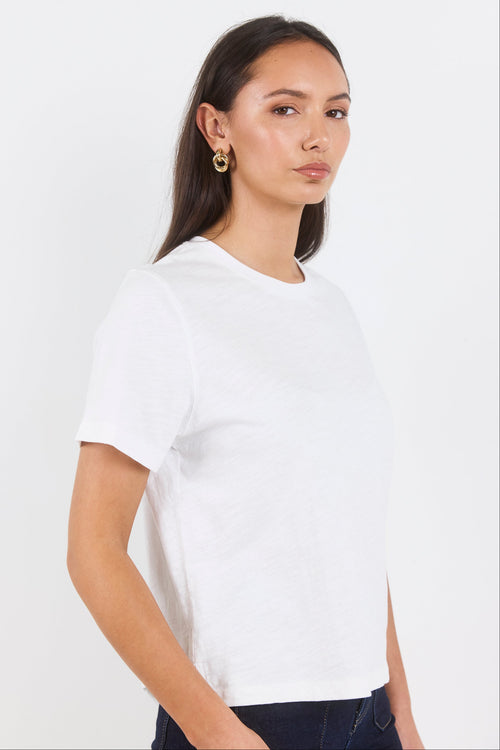 A woman wearing a plain white short-sleeve crewneck t-shirt, shown from the side against a clean white studio background.