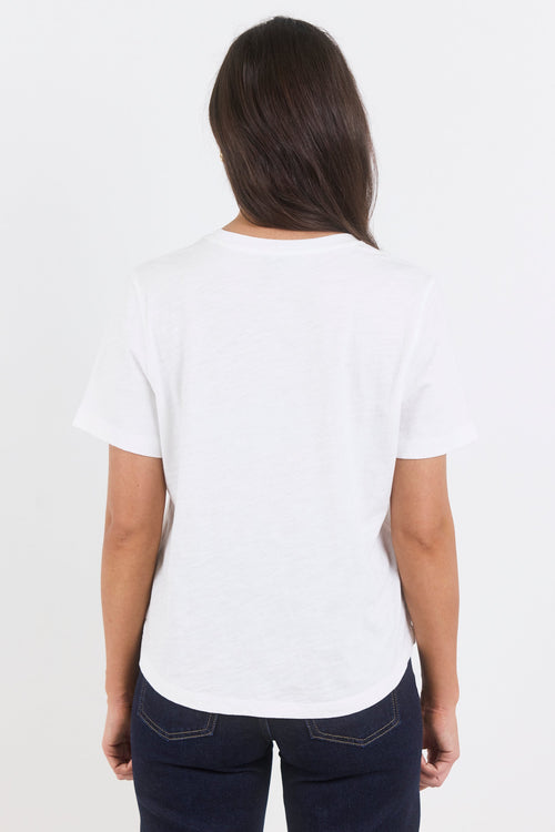 A woman viewed from behind wearing a plain white short-sleeve crewneck t-shirt and dark navy blue jeans against a light gray studio background.