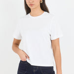 A woman modeling a plain white short-sleeve crewneck t-shirt paired with dark blue jeans, photographed against a clean white studio background.