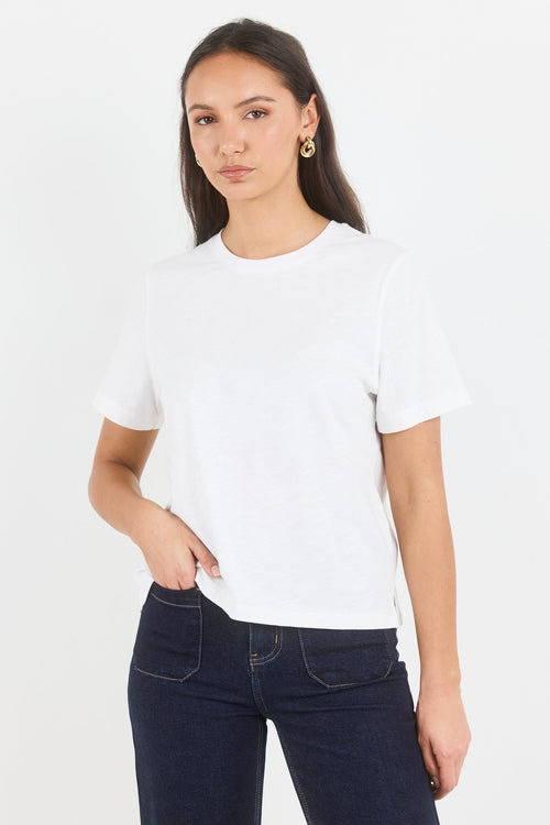 A woman modeling a plain white short-sleeve crewneck t-shirt paired with dark blue jeans, photographed against a clean white studio background.