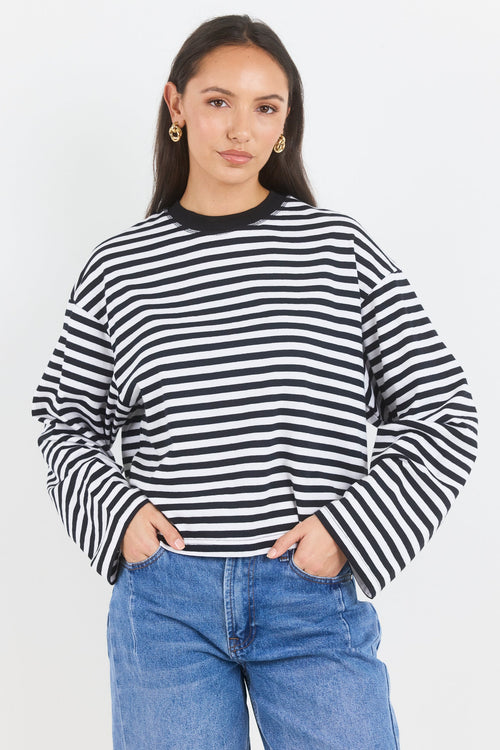 Woman wearing a black and white striped sweater with blue jeans on a white background