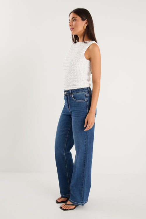 model wears a pair of blue jeans with a white tank top