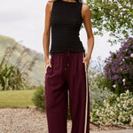 Woman wearing a black sleeveless top and maroon pants with a white stripe outdoors.