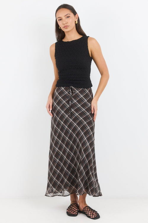Woman wearing a black sleeveless top and plaid skirt on a white background