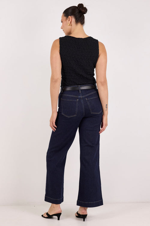 A woman is shown from the back wearing dark navy wide-leg jeans, a black sleeveless top, and black heels against a plain white studio background.