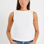 Woman wearing a white sleeveless textured top with a fitted silhouette and high neckline, paired with high-waisted denim jeans.