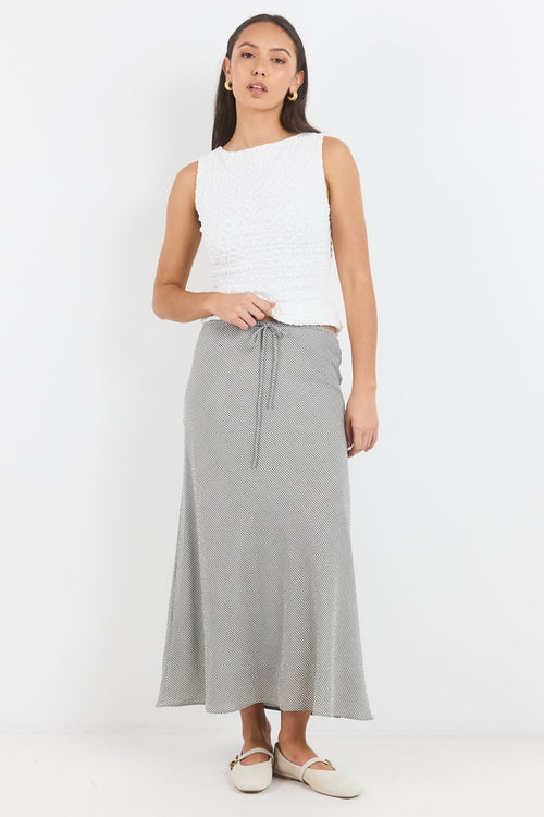 Woman wearing a white sleeveless top and gray skirt on a white background
