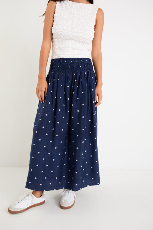 Model wearing a navy polka dot maxi skirt with a shirred elastic waist and a flowy silhouette.