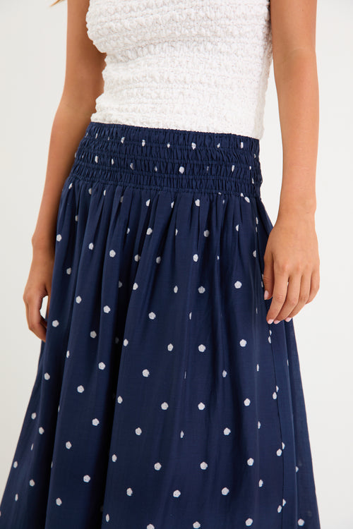 Model wearing a navy polka dot maxi skirt with a shirred elastic waist and a flowy silhouette.