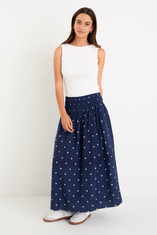 Model wearing a navy polka dot maxi skirt with a shirred elastic waist and a flowy silhouette.