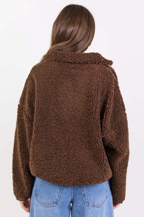 Person wearing a brown teddy jacket and blue jeans on a white background
