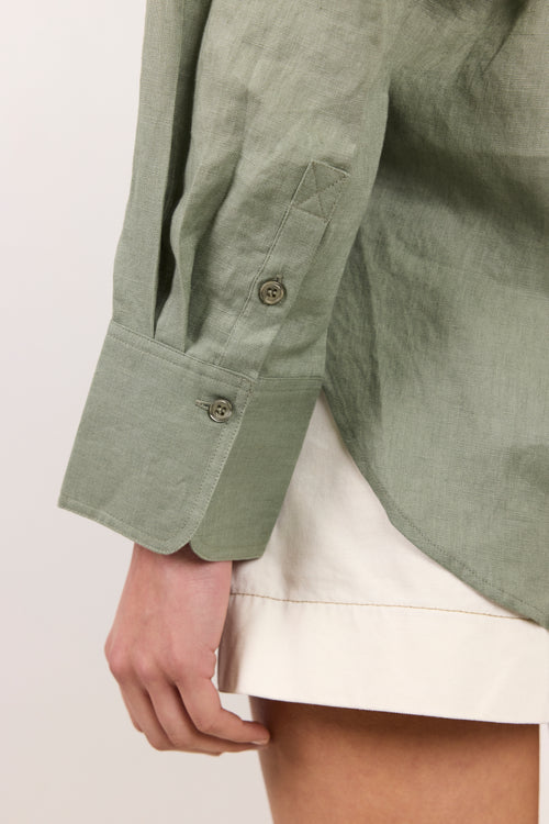 Close-up of a person wearing a sage green linen button-up shirt with a chest pocket and a cream-colored skirt or shorts.