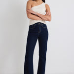 model wears dark blue jeans and one shoulder cream tp with beige heels