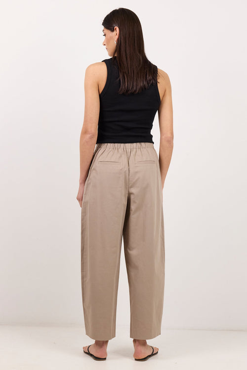 A woman is shown from behind wearing beige wide-leg cropped pants, a black sleeveless top, and black sandals against a plain white studio background.